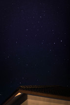 stars in a night sky above a roof 