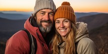 Portrait of smiling couple in winter clothes looking at camera on top of mountain