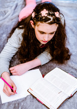 teen girl reading a Bible and writing in a journal 