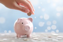 Female hand putting coin into piggy bank on bokeh background