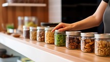 Woman holding glass jars with different kinds of nuts on shelf in kitchen