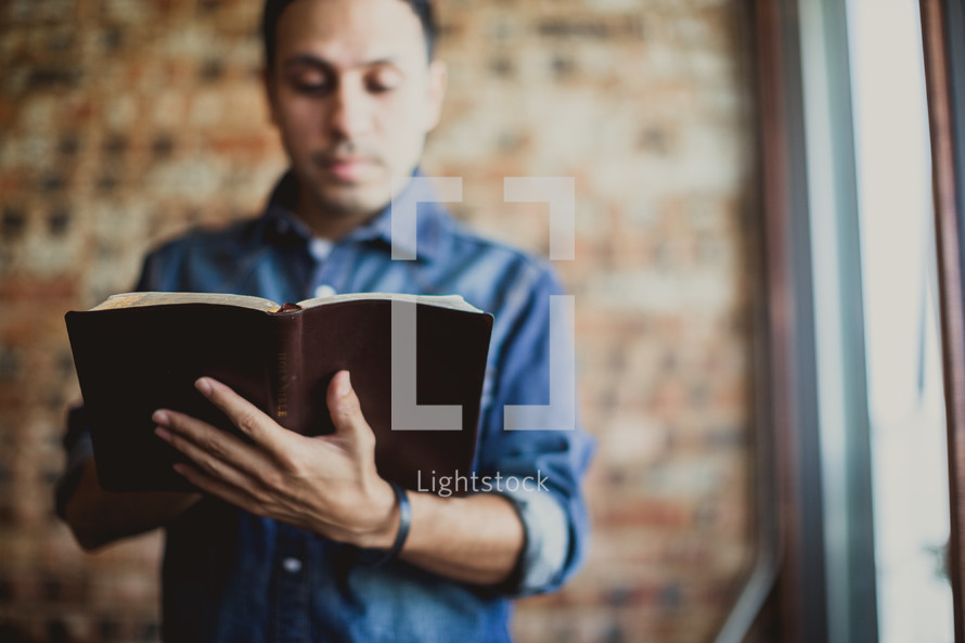 Latino man reading a Bible standing 