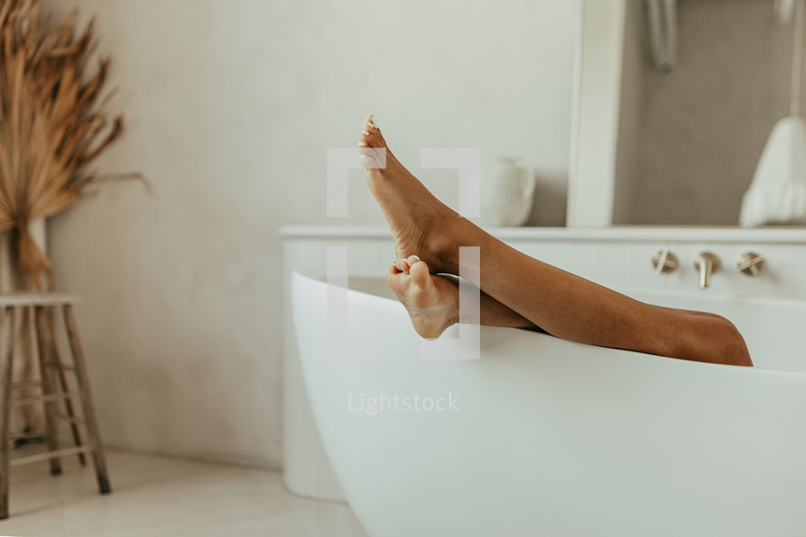Woman's feet hanging over bathtub in bathroom