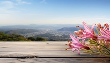 Pink lily flowers on wooden table with mountains and blue sky background
