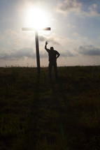 a man praying in front of a cross with hand raised 