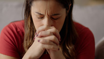 Religious adult girl in 30s Praying to God, Hands Clenched at Home
