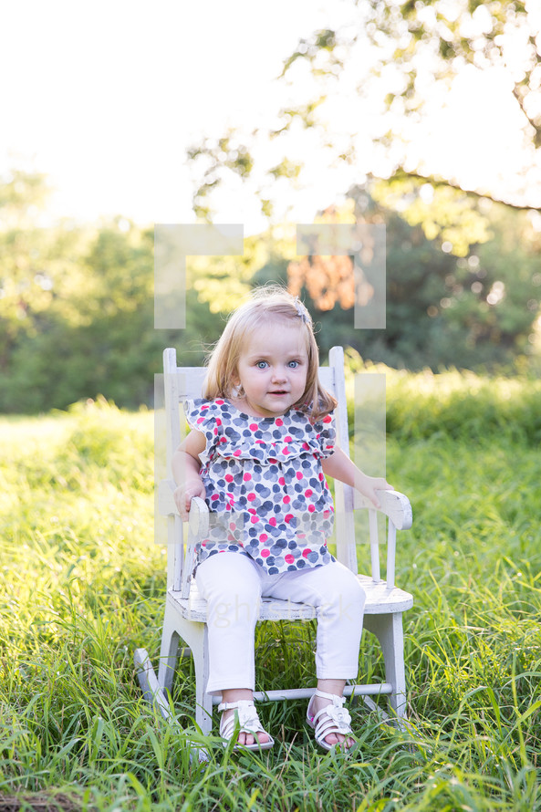 a toddler sitting in a chair in the grass