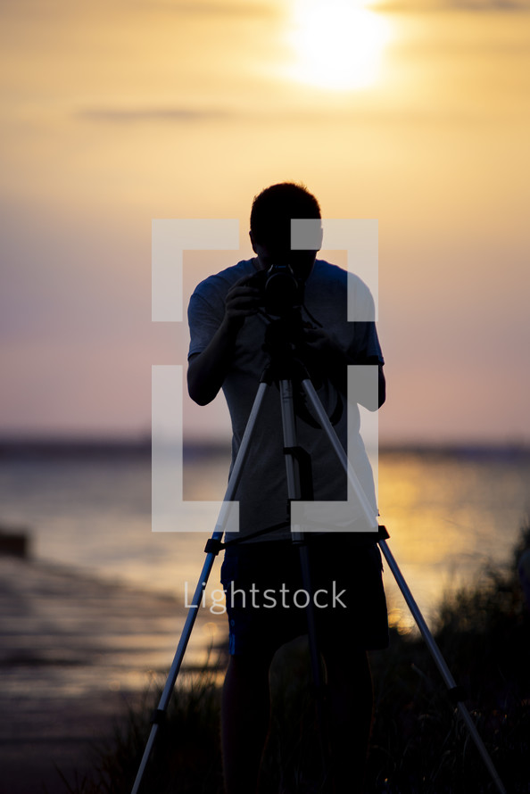 man with a camera and tripod standing on a beach 