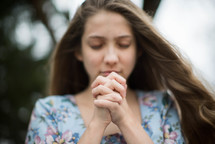 A young woman praying with her hands clasped.