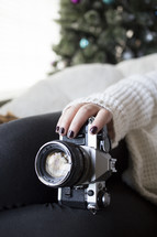 a woman holding a camera on her lap with a Christmas tree in the background 
