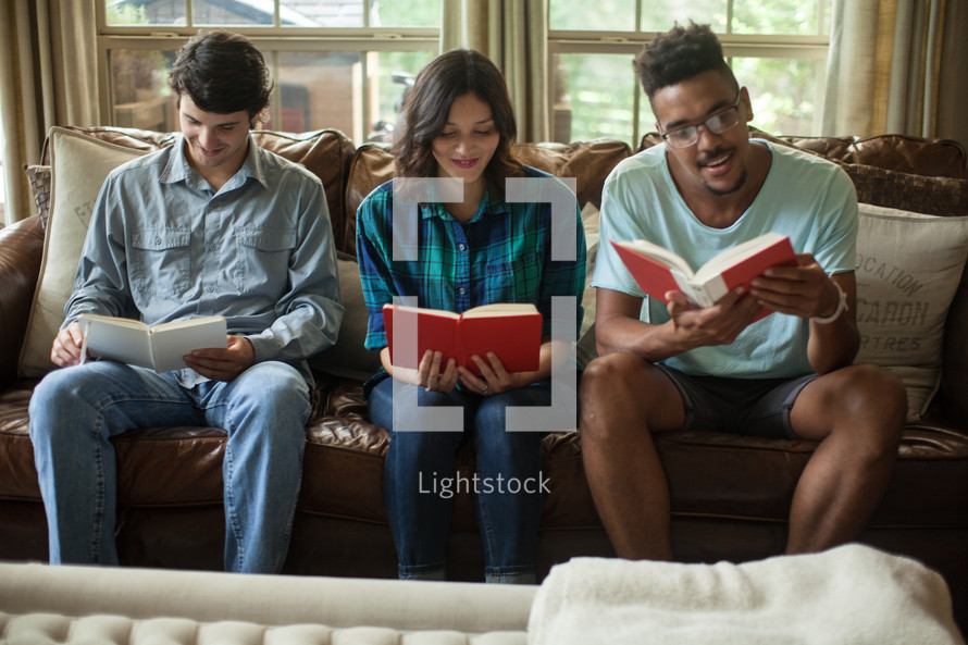 Three young people sitting on a couch and studying the Bible.