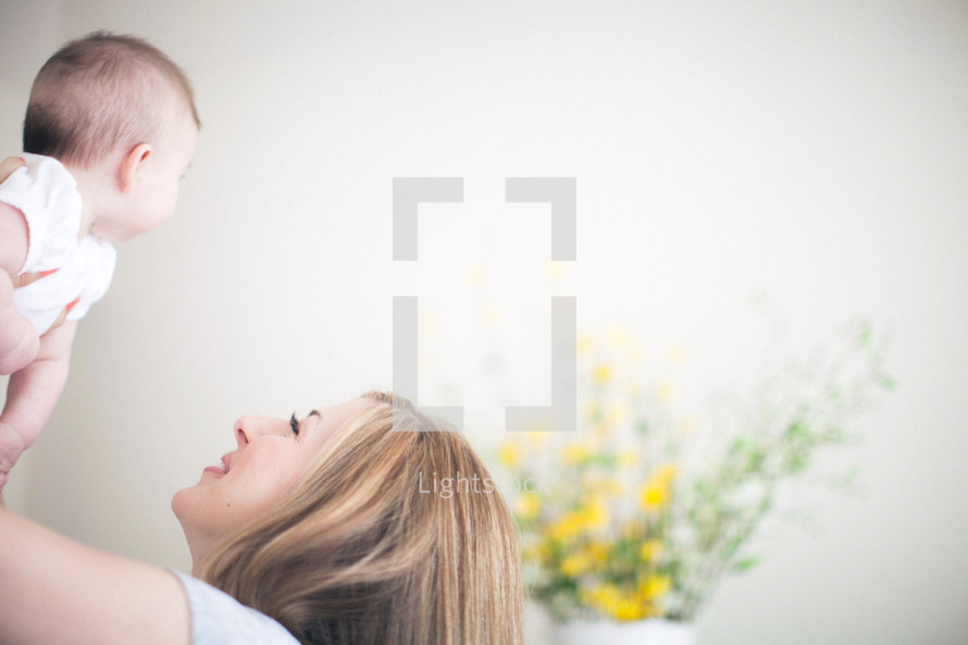 Mother holding daughter in the air with yellow flowers in the background.