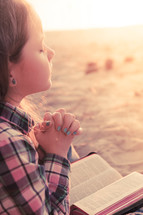 young girl praying on the beach with her bible in her lap at sunset; thinking, hearing from God
