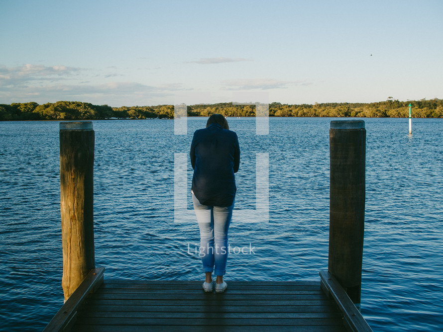 a woman standing at the edge of a pier looking down at the water 
