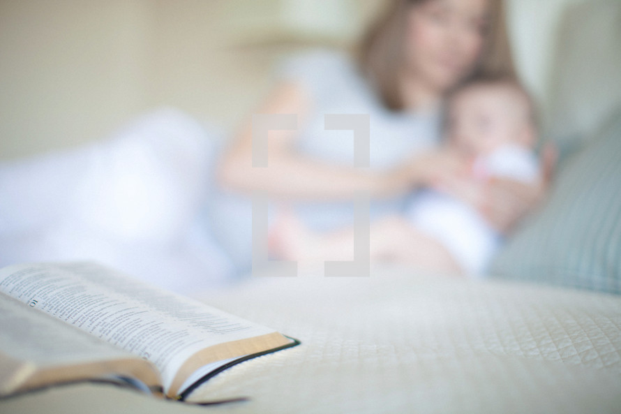 Mother and infant daughter laying on the bed with an open Bible.