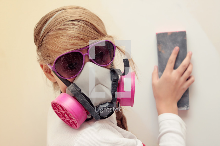 teenage girl sanding a wall with mask and goggles