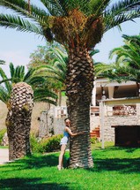 Beautiful young woman or teen age in denim shorts hugging palm tree in Greece. Vacation time.