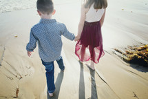 sibling walking holding hands on a beach 