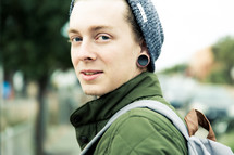 A young man in a winter cap and ear lobe plugs.