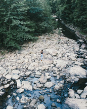 woman walking on rocks along a stream 