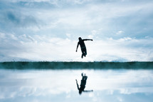 man jumping in the field and reflecting in the lake