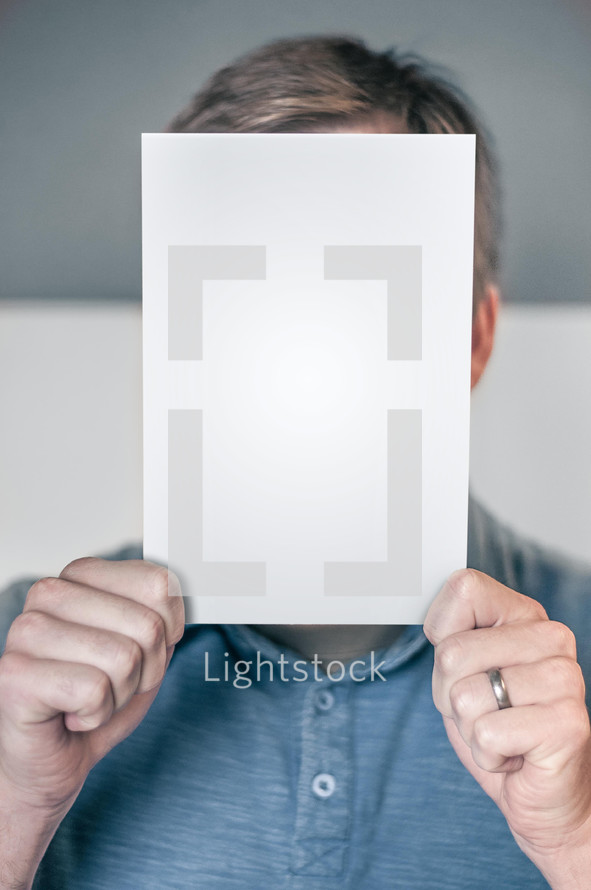 Man holding up a blank page or book cover hiding his face.