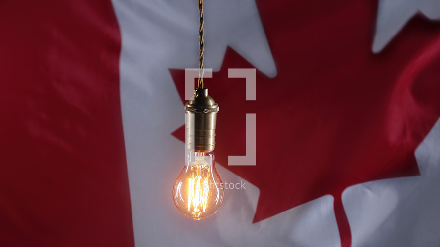 Flickering classic antique Edison Tungsten filament lamp on waving canadian flag background. 