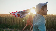 Cute little boys - American patriotic kids running with national flag on open area countryside road.
