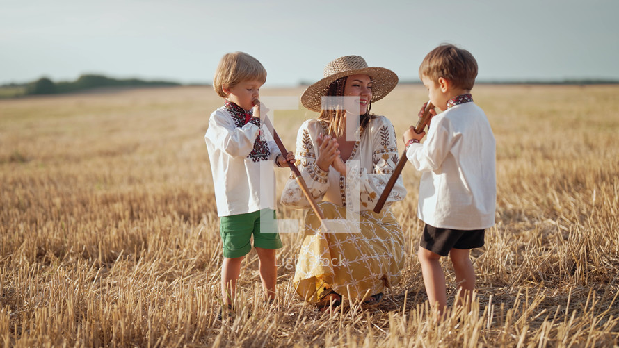 Boys playing on wooden flutes - sopilka. Ukrainian mother with children sons in wheat field. Woman in embroidery vyshyvanka. Ukraine, traditional music instrument, melody, song