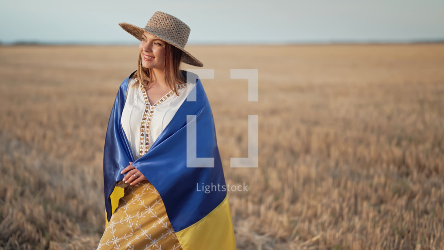 Smiling ukrainian woman with national flag in wheat field after harvesting. Charming rural lady in embroidery vyshyvanka. Ukraine, independence, freedom, patriot symbol, victory in war.