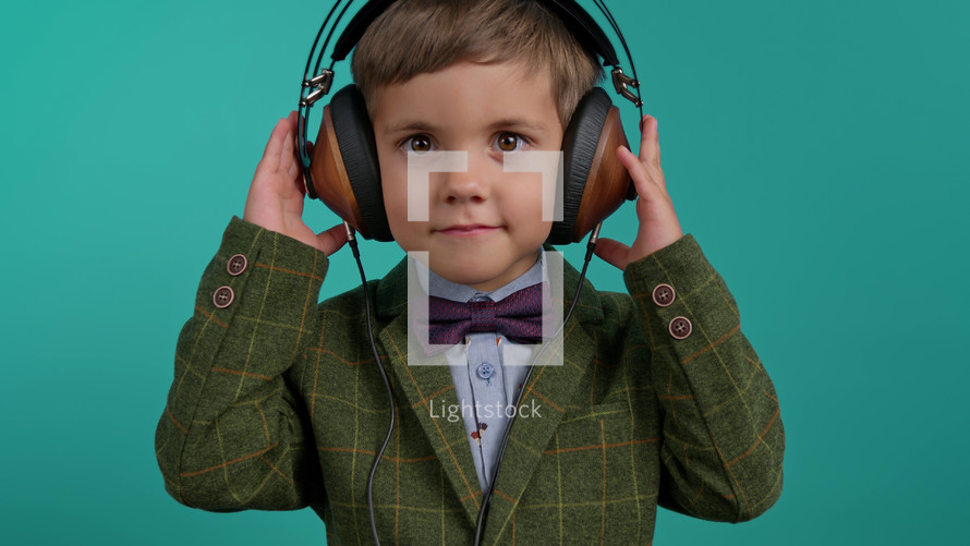 Handsome little toddler boy listening to music with old headphones, child having fun, funny dancing in studio on blue background. Dance, radio, analog concept.