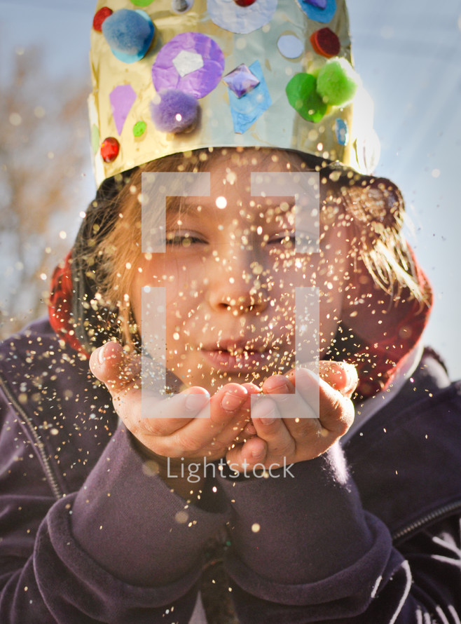 a child dressed as a king blowing glitter 