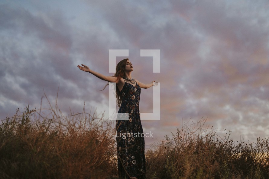 a woman with outstretched arms at sunset 