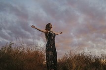 a woman with outstretched arms at sunset 
