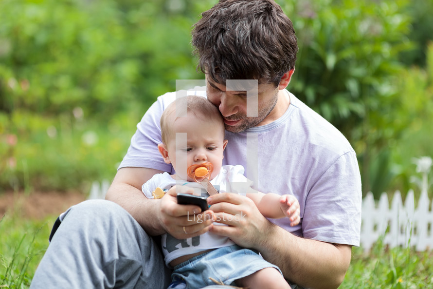 Father holding a baby and texting on his mobile
