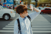 teen boy crossing a city street and shading sunlight from his eyes 