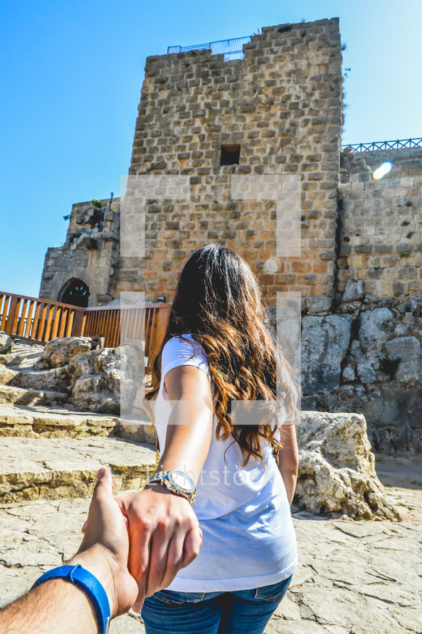 woman leading a man towards castle ruins 