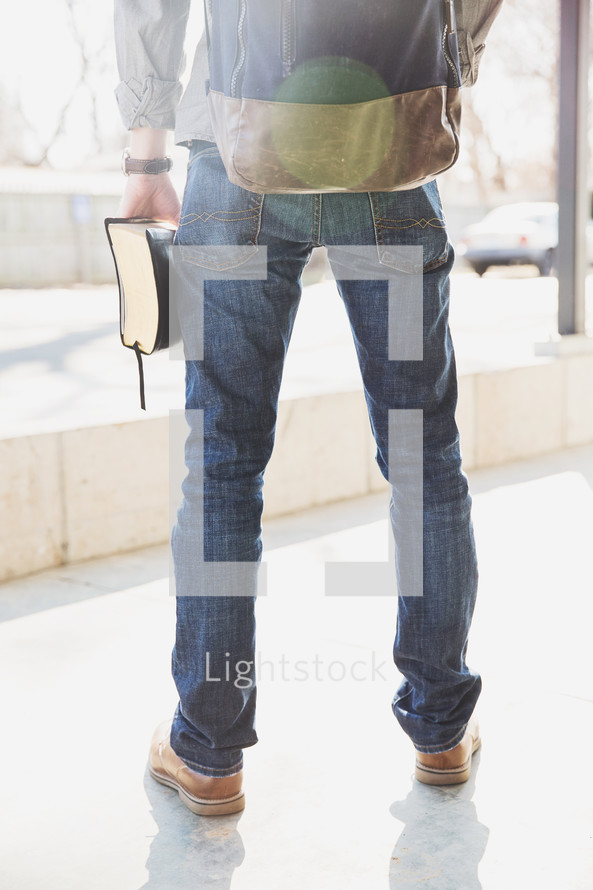 man with a backpack holding a Bible at his side 