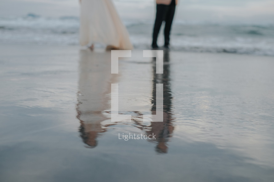 reflection of a bride and groom in wet sand 
