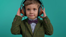 Handsome little toddler boy listening to music with old headphones, child having fun, funny dancing in studio on blue background. Dance, radio, analog concept.