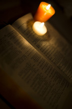 Open Bible with two votive candles on corner of pages.