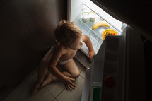 Little boy sitting near open fridge at night