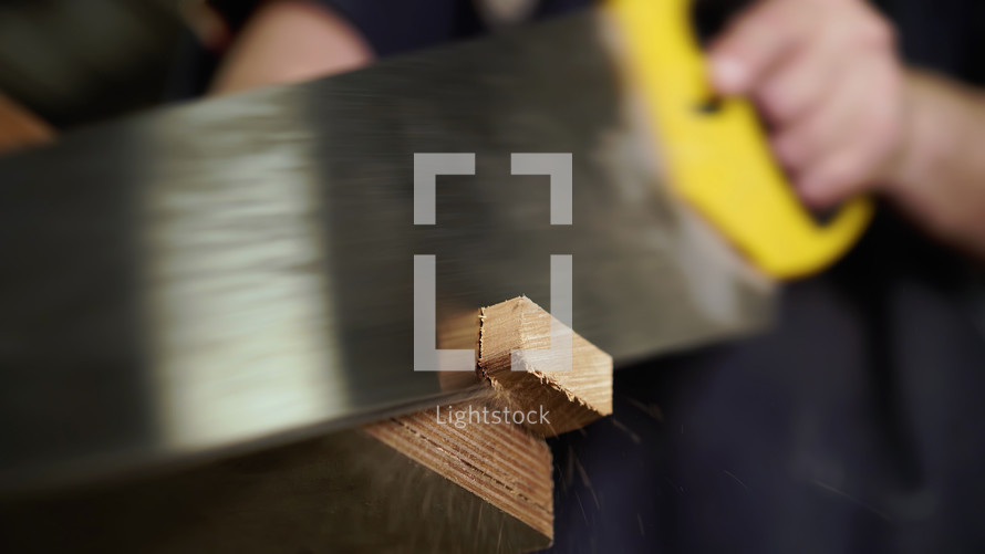 Handwork concept, woodworking workshop. Carpenter saws wooden board with hand jigsaw. Close-up view.