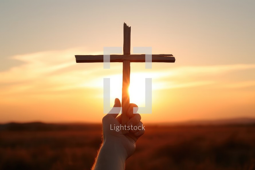 A person holds a cross in his hand against the background of the setting sun.