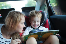 Boy holding book sitting in a car with mother