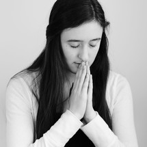 A young woman praying with hands folded.