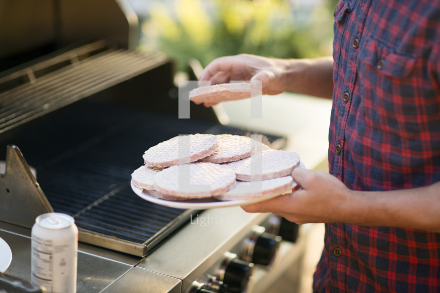 man putting hamburgers on the grill 