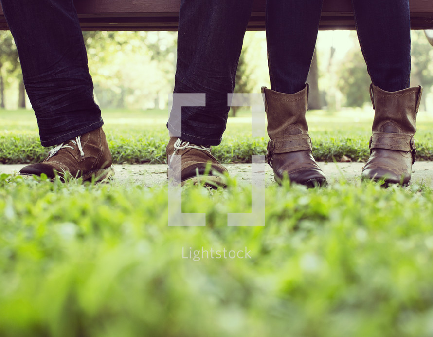 feet of a couple in boots sitting on a bench 