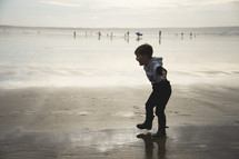 a boy splashing in wet sand on a beach 