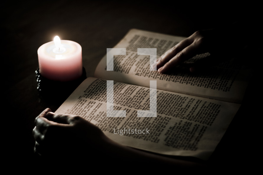 man reading a Bible with candlelight 